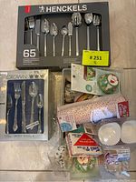 Henckels 65-piece cutlery set boxed along with Crown 24-piece silverware set and various baking supplies such as cupcake liners and bags.