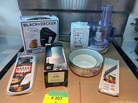 Photo showing Braun food processor, Black & Decker mixer box, white floral bowl, and kitchen utensils on countertop.