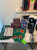 Photo showing multiple boxed light sets, outdoor garland, stockings with poinsettia design, light projector and some small accessories on a table.