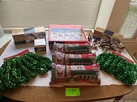 Complete lot including boxed Christmas village set, loose pillows, and green tinsel garlands on a table
