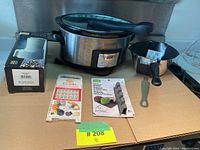 Photo showing Crock Pot slow cooker, boxed electronic grater, spice holder set, and knife holder with knives on a tabletop.