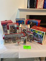 Lot consisting of multiple boxed and unboxed Christmas village items including porcelain lighted house, figurines, and accessories arranged on a table.