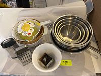 Kitchenware lot including nested stainless steel mixing bowls, colander, graters, plastic strainers, bowls and biscuit cutters.