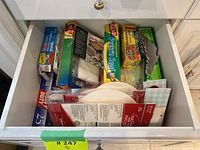 Plastic and aluminum wraps, with disposable bowls and other kitchen items seen from above in open drawer.