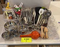 Full overview of kitchen items including stainless steel bowls, utensils, glass bowls, wooden reamers, and various smaller kitchen tools in plastic bin.