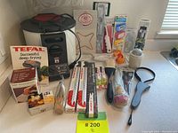 Photo showing boxed Tefal electric deep fryer with instruction manuals and assorted kitchen utensils including mallet, peelers, metal skewers, and others