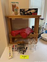 Wide view of the lot on a wooden shelf showing four wine glasses, red wine bottle sleeves, boxed Frosty Mug, boxed Philips wine opener, and assorted small accessories in front of shelf