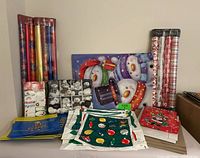 photo showing multiple rolls of Christmas-themed wrapping paper, assorted gift bags, and packaged gift wrap accessories grouped together