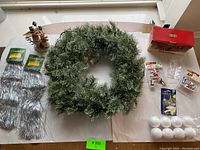 Top view of all items including wreath, tinsel garlands, white foam balls, and figurines arranged on table