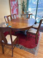 Photo showing six wooden dining chairs surrounding a wooden dining table, with white upholstered seats visible.