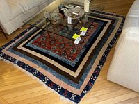Photo showing the entire Turkish area rug under a glass-top coffee table, displayed on hardwood flooring between light-colored sofas.