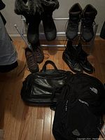 Photo showing three pairs of women's boots and two bags on a hardwood floor. The boots appear to be size 41, including one pair with fur trim. The bags include a black leather one and a black backpack.