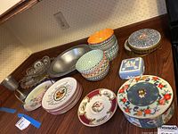 Wide view showing all assorted plates, bowls, glass platter, decorative boxes and metal bowls on countertop.