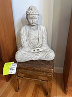 Buddha statue sitting cross-legged on top of wooden bench against wall.