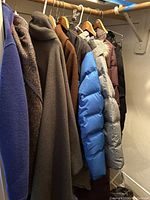 Side view showing several wool and puffer jackets in brown, blue, silver, and purple hung on a rod.