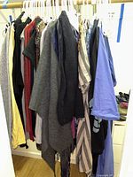 Photo showing multiple clothing items hanging on rack including a gray poncho and other jackets and sweaters.