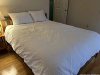 Front view of bed made up with white bedding, fitted sheet, and two pillows.