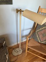 Full view of the cream-colored vintage metal floor lamp with adjustable arm positioned near a wooden chair.