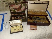 Three open jewelry boxes with assorted jewelry pieces and cufflinks placed inside and on top.