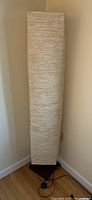 Front-left view of the tall floor lamp with textured cream paper shade and square wooden base.