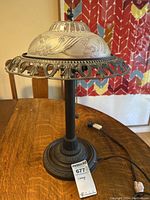 Front and side view of vintage metal table lamp with frosted glass shade and floral motifs on a wooden table.