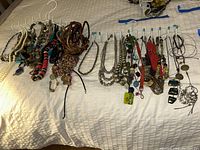 Overview of all necklaces hanging on white hooks, with a variety of beads, faux pearls, leather cords and pendants visible.