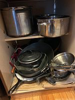 Lower shelf shows mixed pans including glass lided frying pan and cast-iron skillet