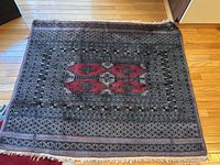 Full view of the rectangular vintage Pakistani rug on a hardwood floor, showing its general color scheme and pattern.