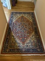 Full view of rectangular decorative area rug with central medallion pattern in rust, navy, cream, and green tones. Shows overall design and size.