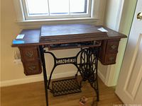 Side view of the antique Singer sewing machine with wooden cabinet and visible metal base with treadle and drawers on each side.