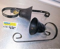 Both black antique farmhouse door bells shown side by side laid flat against a surface, showing overall shape and mounting brackets.