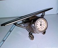 Front angle view showing the silver metal high wing airplane desk clock with clock face visible, on small wheels.