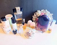 Photo of multiple vintage perfume bottles including a large purple gradient bottle, smaller bottles with floral caps, and lace decorative sachets.