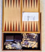 Open wooden box showing backgammon board inside lid, chess pieces, checkers, dice and instructions in compartments below board