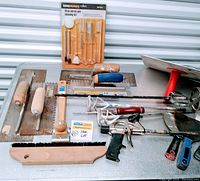 Full overview of the lot arranged on a surface showing spread of items including trowels, putty knives, scrapers, cleaning kit, hawk and mixing paddle.
