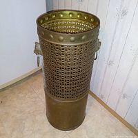 Tall cylindrical brass and copper umbrella stand with woven lattice metal pattern, shows side ring handles and riveted upper rim