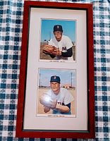 Full view of the framed item showing both player photos stacked vertically inside a reddish wood frame with matting on a checkered tablecloth.