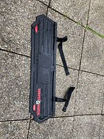 Black rectangular Bumper Badger rubber protector lying on pavement showing embossed text and pattern.