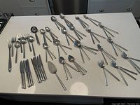 Full view of all flatware pieces spread out on countertop showing the variety and quantity of forks, spoons, knives, and serving utensils.