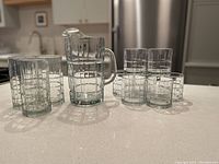 View of all glassware including one water pitcher, three tall glasses, and seven short glasses, showing the cross etched pattern on each item.
