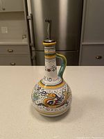 Front view of the hand-painted olive oil bottle with spout on a white kitchen countertop.