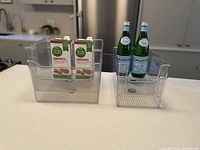 Two large and four small clear plastic storage bins displayed on a kitchen counter with almond milk cartons and San Pellegrino bottles inside to demonstrate size and use.