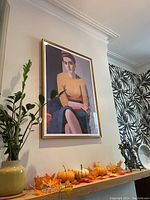Full view of the framed poster hanging on a wall, showing the pensive woman figure and part of a decorative environment with plants and small pumpkins.
