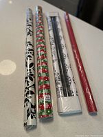 Six assorted gift-wrapping paper rolls unopened in original plastic, showing a variety of patterns including floral, festive, damask, solid colors.