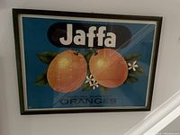Framed vintage-style Jaffa Oranges print on blue background with green frame hung on wall.