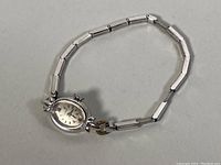 Overview of entire watch laid flat, showing oval case and stretch band