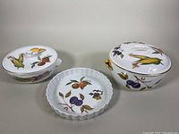 Set of three Royal Worcester Evesham cookware pieces: one quiche/tart pan and two lidded casserole dishes with colorful fruit designs on white porcelain.