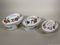 Three Royal Worcester Evesham lidded oval casserole dishes of varying sizes arranged in a row showing fruit decorations.
