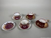Photo showing four Royal Doulton teacups and saucers including an extra saucer. Burgundy and white cups with intricate gold floral gilding. Very good vintage condition. Minor wear visible on close inspection.