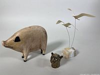 Photo of three items: carved wooden animal figurine, signed Takashi leopard head sculpture, kinetic seagull sculpture on marble base.